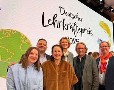 Drei Frauen und drei Männer stehen vor einer großen Wand mit der Aufschrift "Deutscher Lehrkräftepreis 2025"