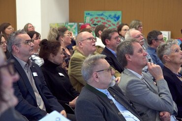 Mehrere Menschen in Sitzreihen schauen interessiert nach vorne.