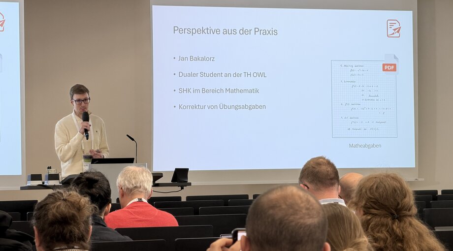 Ein Student steht im Hörsaal vor Publikum und spricht ins Mikrophon.