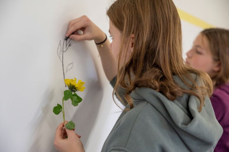 Eine Schülerin hält eine Blume in der Hand und versucht diese auf einer Tafel nachzumalen.