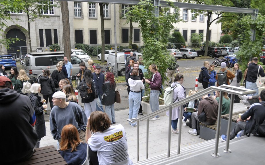 Studierende sitzen auf der Eingangstreppe vor dem katho-Hochschulgebäude.  