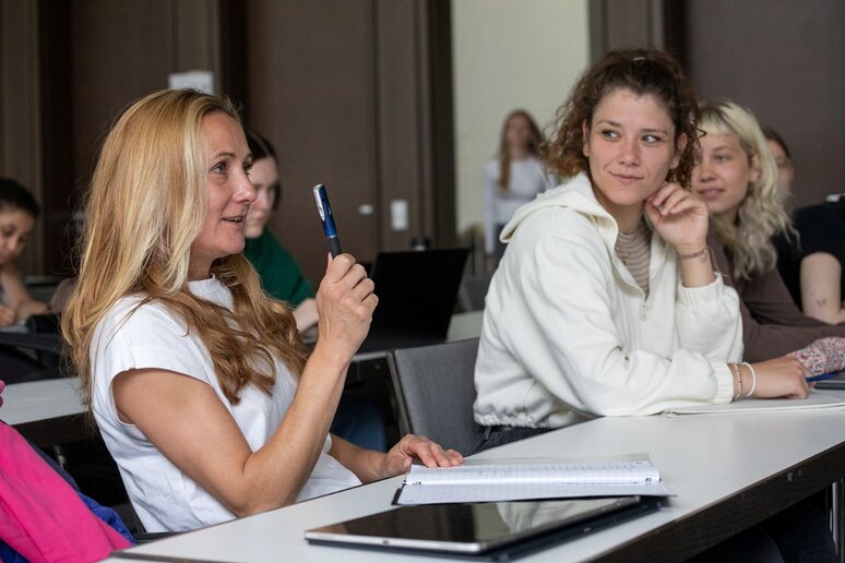 Studierende im Gespräch. Eine blonde Frau hebt ihren Stift und spricht nach vorne.