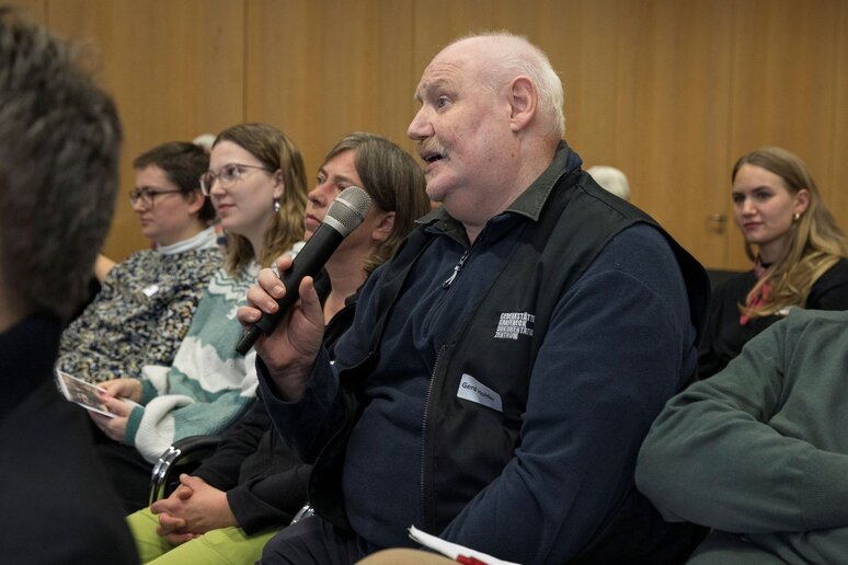 Ein Mann aus dem Publikum stellt eine Frage. Er hat das Mikrofon in der Hand.