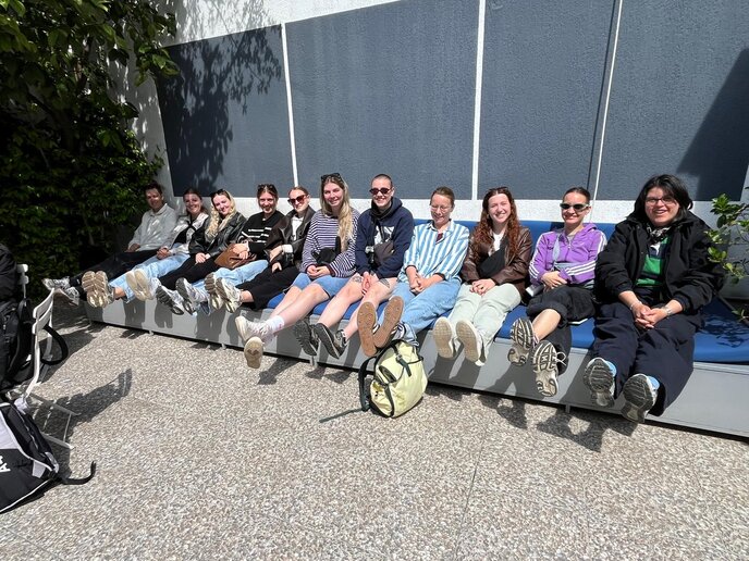 Studierende sitzen draußen auf einer Bank in der Sonne