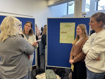 Studierende stehen vor einem Poster und diskutieren.