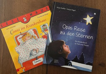 Zwei Kinderbücher mit den Titeln "Conni im Krankenhaus" und "Opas Reise zu den Sternen" liegen auf einem Tisch.