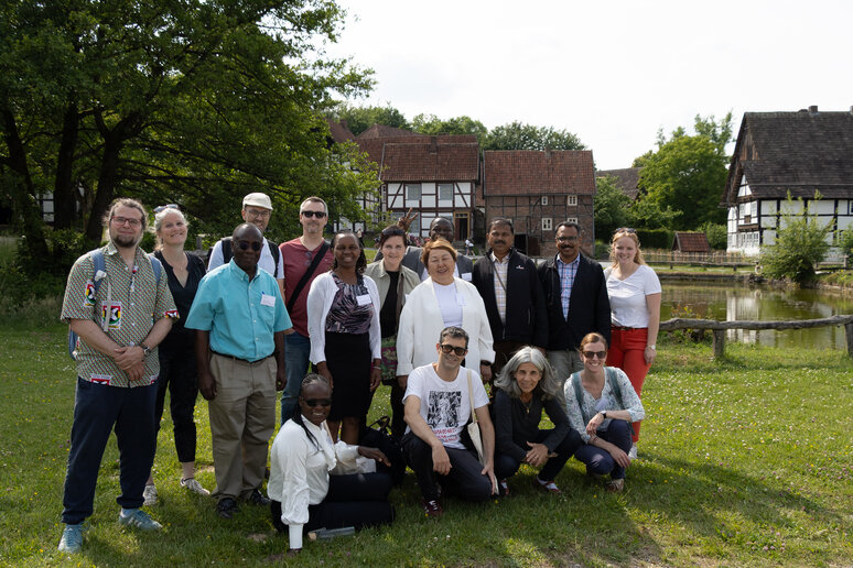 Eine Gruppe von Menschen steht zusammen und wird fotografiert. Sie stehen auf einer Wiese und sind fröhlich und lachen in die Kamera. 