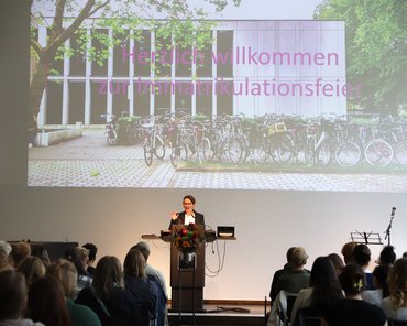 Die Dekanin steht am Pult und begrüßt die neuen Studierenden.