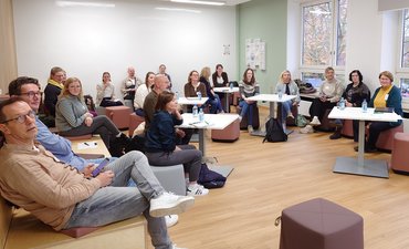 Anleiter_innen sitzen zusammen in einem Seminarraum.