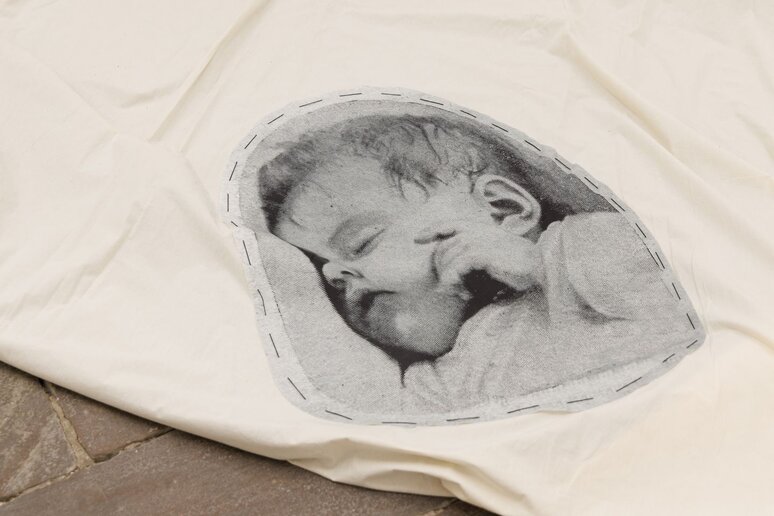 Auf einem weißen Tuch ist eine schwarz-weiß Abbildung einen Babys gestickt.