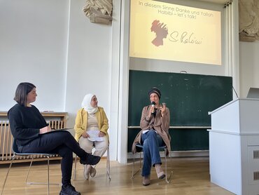 Drei Frauen sitzen im Halbkreis auf Stühlen und unterhalten sich.