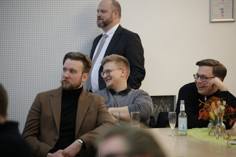 Publikum sitzend und ein Mann an der Wand lehnend