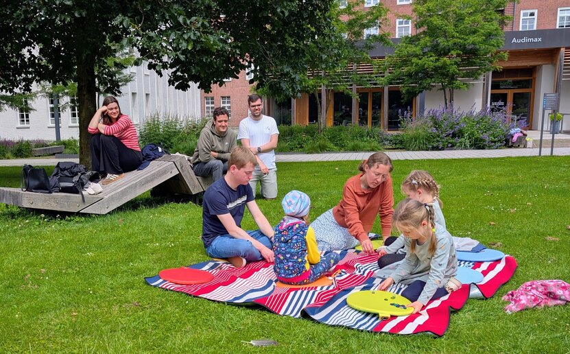 Die Kinder sitzen auf einer Decke und zählen Murmeln unter Anleitung der Studierenden.
