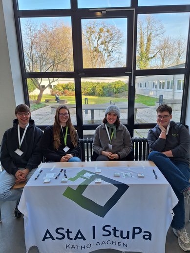 Vier Vertreter_innen des AStAStuPa sitzen am Infostand