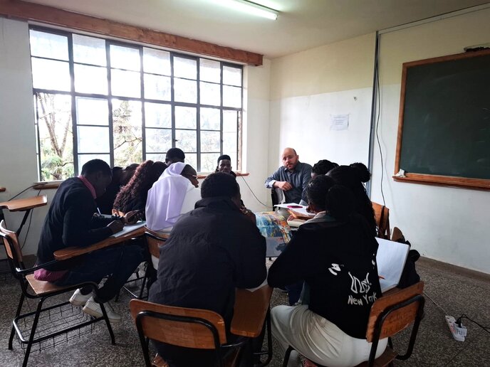Mehrere kenianische Studierende sitzen in einer Gruppe zusammen in einem Seminarraum. Ihnen zugewandt sitzt Sebastian Rost.
