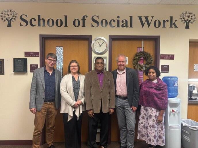 Fünf Personen stehen für ein Gruppenbild vor einem Eiongang mit der Aufschrift "School of Social Work".