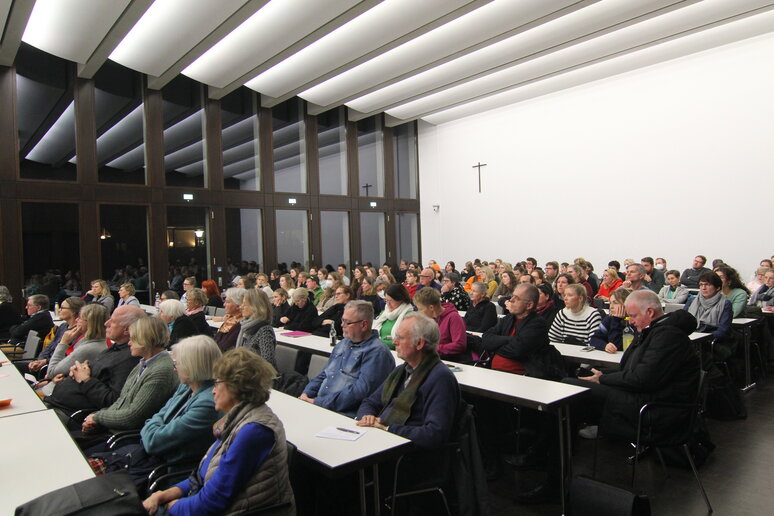 Ein Hörsaal mit vielen Zuschauern, die in Reihen sitzend dem Vortrag zuhören.