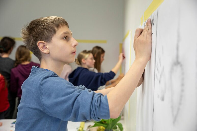 Schüler:innen malen mit Kohle auf an der Wand befestigtem Papier.