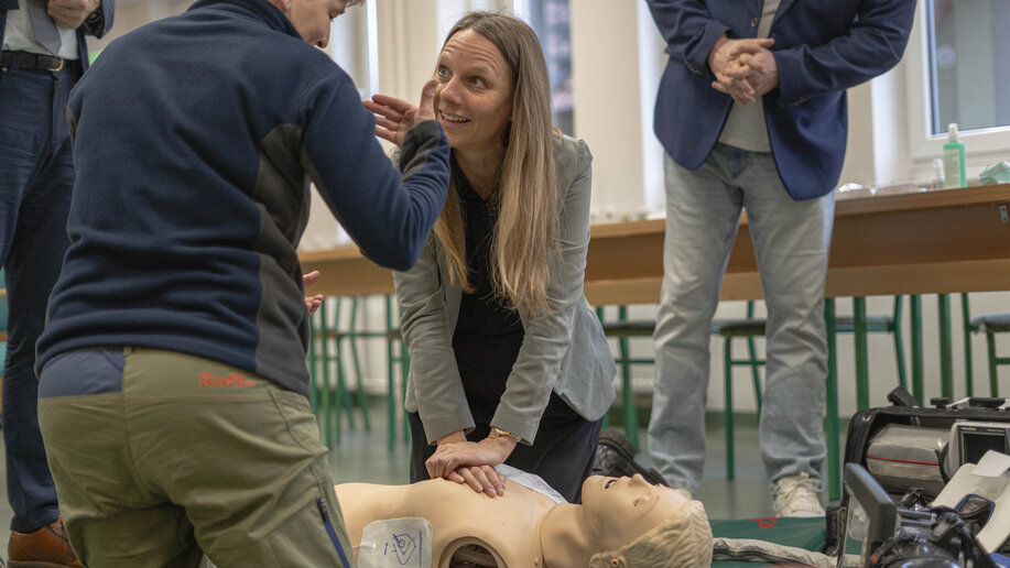 Lisa Jungkamp kniet vor einer Reanimationspuppe und übt Wiederbelebung. Eine Fachperson erklärt die Übung.