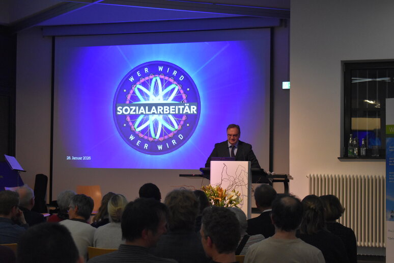 Im Hintergrund sieht man auf der Leinwand eine Folie mit dem Schriftzug "Wer wird Sozialarbeitär" in Anlehnung an das Layout von Wer wird Millionär. Vorne steht ein Mann am Rednerpult.