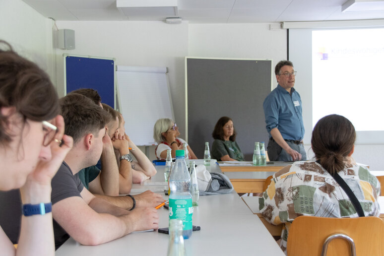 Teilnehmende sitzen in einem Seminarraum an Tischen