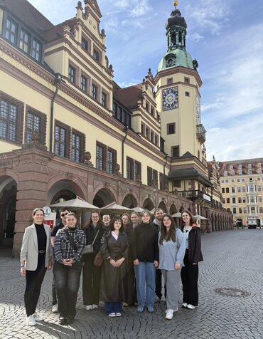 Elf Studierende und ihre Professorin stehen als Gruppe vor einem repräsentativen historischen Gebäude.