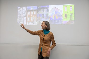 Diane Samuels steht vor einer Reihe von künstlerisch gestallteten Häusern.
