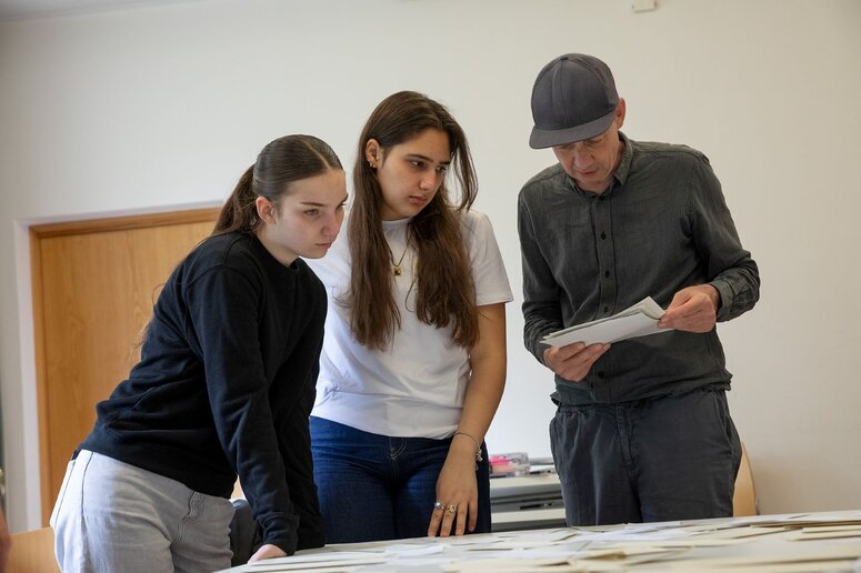 Drei Personen schauen auf einen Tisch, auf dem verschiedene Papiere liegen.