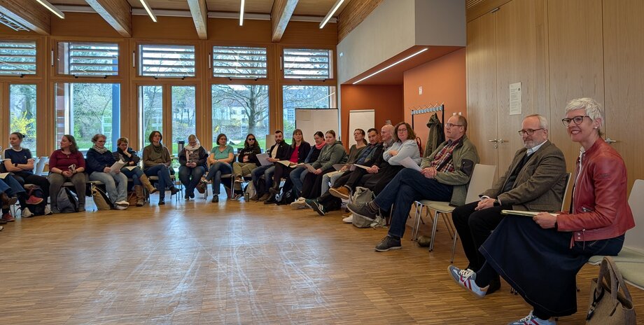 Die Teilnehmer_innen sitzen sich im Stuhlkreis gegenüber.