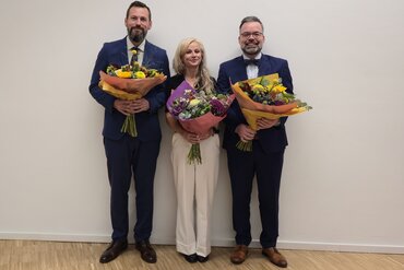 Prof. Dr. Robin Junker, Prof.in Dr.in Ulrike Kuhn, Prof. Dr. Markus Barth (v.l.n.r.) mit Blumen in den Händen.