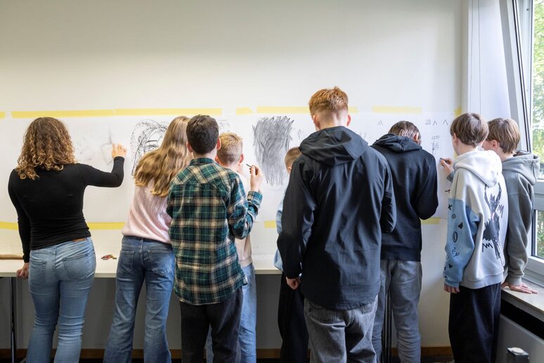 Eine Gruppe Schüler:innen malt mit Kohle auf Papier, welches an der Wand befestigt ist.