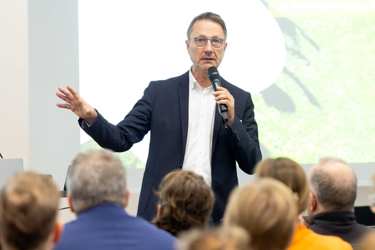 Moderator Uwe Schulz spricht mit Mikrophon zu den sitzenden Gästen.