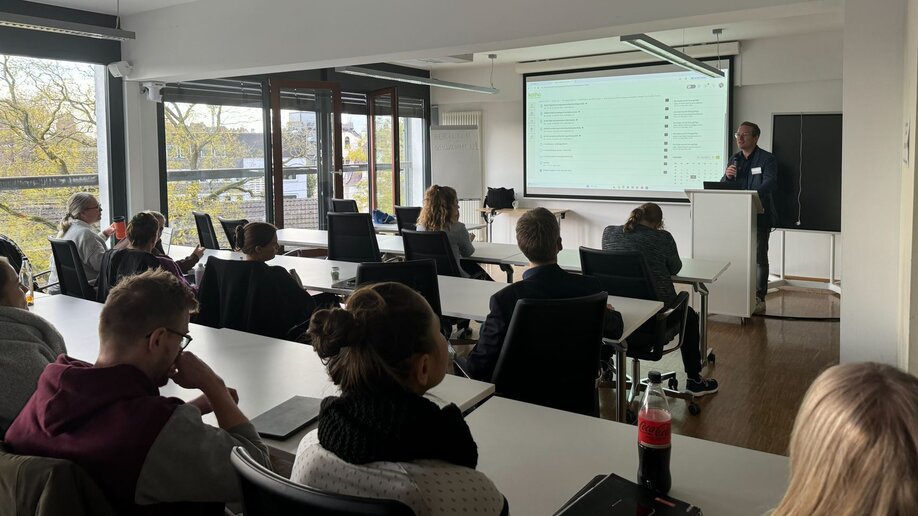 Prof. Dr. Oliver Tiemann hält eine Vorlesung, in den Reihen sitzende Studierende hören zu.