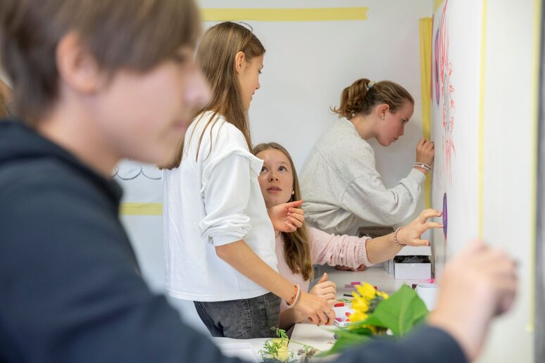 Schüler:innen malen mit Kohle auf an der Wand befestigtem Papier.