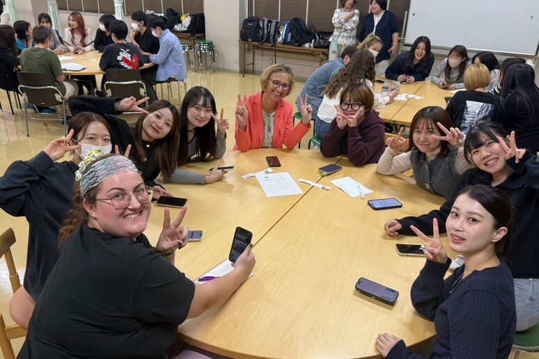 Eine Gruppe japanischer Studierender sitzen mit Rektorin an einem runden Tisch und lächeln in die Kamera.