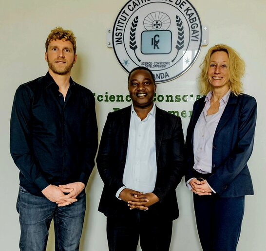 Felix Nuss, Fidèle Dushimimana und Angela Wernberger vor dem Logo des Institut Catholique de Kabgayi 