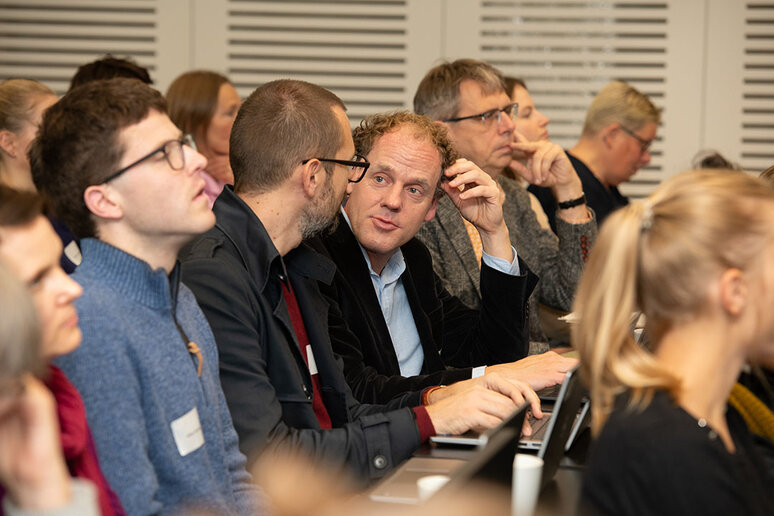 Teilnehmende in Sitzreihen unterhalten sich.