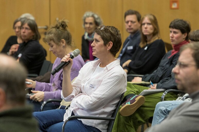 Eine Frau aus dem Publikum hält das Mikrofon, um eine Frage zu stellen.