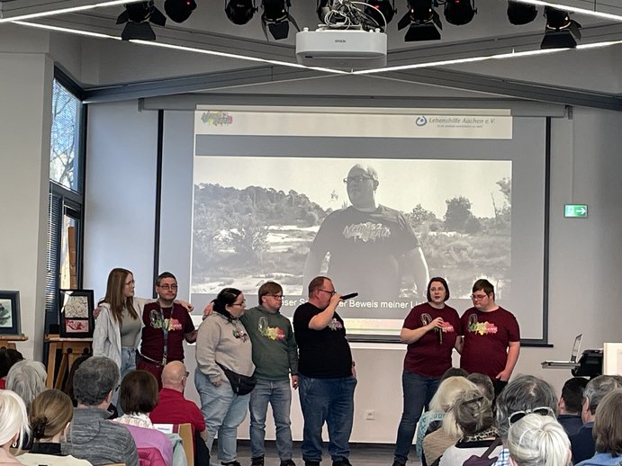 Die Bandmitglieder stehen auf der Bühne, im Hintergrund ist eine Leinwand, wo ein Musikvideo läuft.
