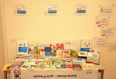 Auf einem Tisch werden zahlreiche Bücher präsentiert. Auf der Tischdecke steht "Starke Kinder - gute Freunde".