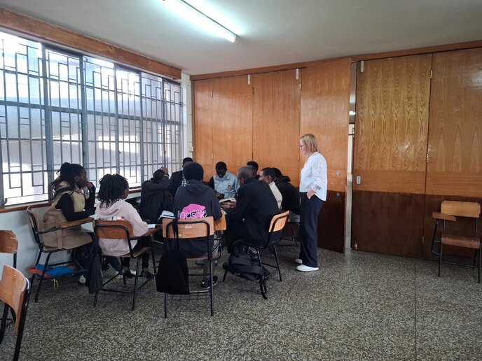 Mehrere kenianische Studierende sitzen in einer Gruppe zusammen in einem Seminarraum. Neben ihnen steht Katharina Tewes.