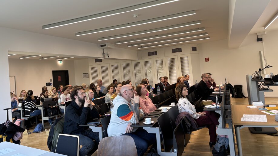Zuhörende sitzen in einem Hörsaal und hören einem Vortrag zu.