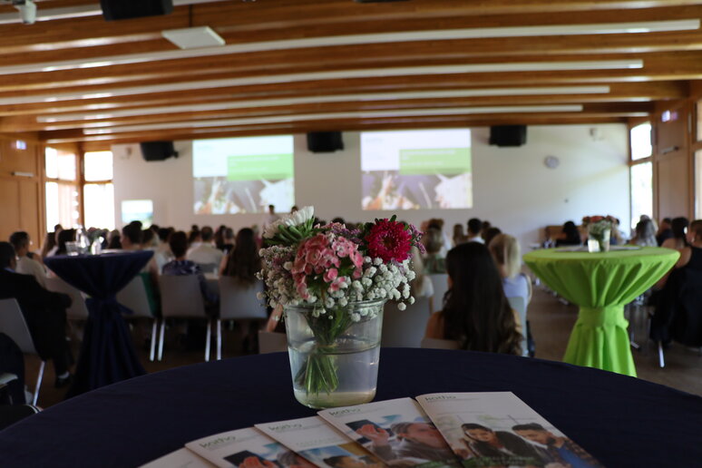 Ein Stehtisch mit Blumen im Hintergrund der Blicke auf die große Menge an Zuschauer_innen.