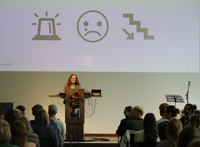 Eine Professorin hält eine Festrede am Pult auf der Bühne.