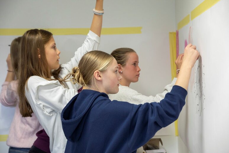 Schüler:innen malen mit Kohle auf an der Wand befestigtem Papier.