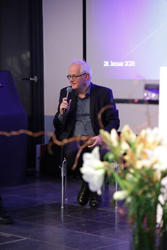 Christof Stock auf der Bühne sitzend, redet zum Publikum