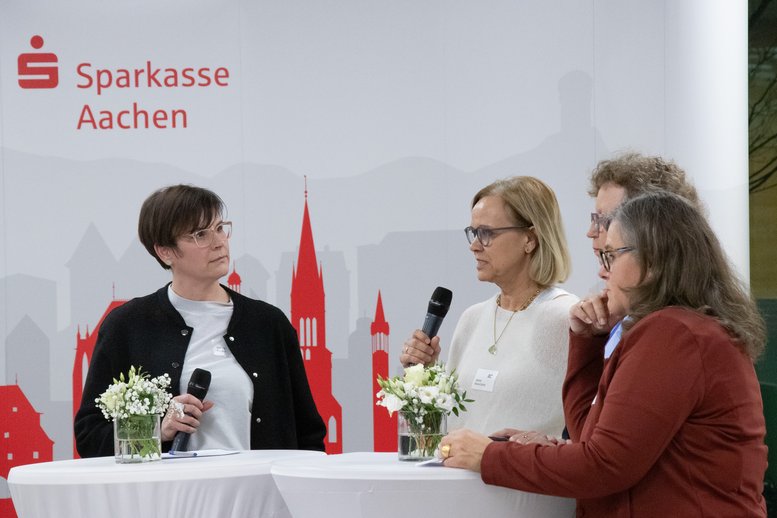 Die vier genannten Frauen stehen gemeinsam mit Mikrofonen an einem Stehtisch. 