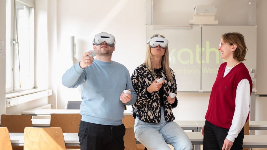 Zwei Personen in einem Seminarraum tragen VR-Brillen, eine weitere beobachtet die beiden.