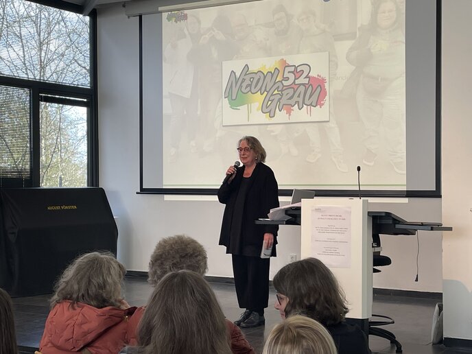 Hilde Scheidt steht auf der Bühne und begrüßt Anwesenden.