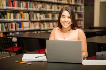 Eine Frau sitzt in einer Bibliothek vor ihrem Laptop.